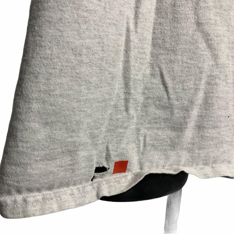 Pode incluir: Uma camiseta cinza com um pequeno furo perto da bainha inferior.