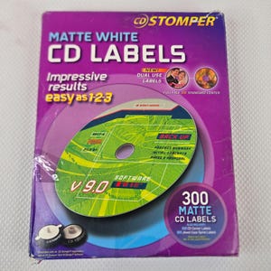 May include: A CD Stomper box with matte white CD labels. The box is purple with white and green text, including "Impressive results easy as 1-2-3" and "300 Matte CD Labels". A CD with green and white graphics is in the center.