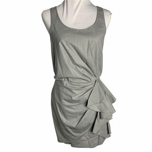 Puede incluir: Un vestido gris sin mangas con un dobladillo con volantes. El vestido tiene un escote redondo y un corpiño ajustado.