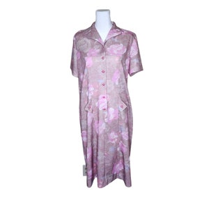 Könnte beinhalten: Ein rosa-beiges Kleid mit Blumenmuster, Kragen und kurzen Ärmeln. Das Kleid hat einen Knopfleisten vorne und zwei Taschen.