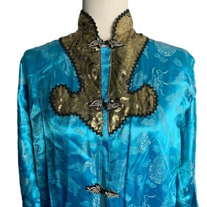 May include: A turquoise blue silk robe with gold and black embroidery. The robe has a mandarin collar and a front closure with decorative buttons.