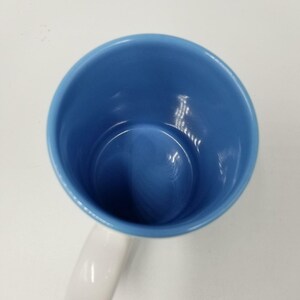 May include: A ceramic mug with a white handle and a blue interior. The mug is empty and viewed from above, showing the inside of the cup. The handle is on the left side of the image.