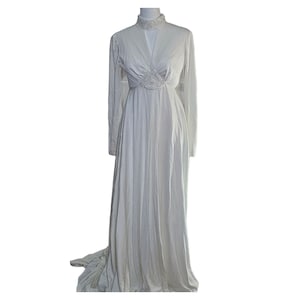 May include: A white long-sleeved gown with a high neckline and a beaded embellishment at the waist.