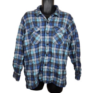 Puede incluir: Camisa de franela a cuadros azules, grises y turquesas con dos bolsillos en el pecho. La camisa de manga larga tiene una botonadura frontal y un cuello cl&aacute;sico. La tela parece suave y c&oacute;moda.