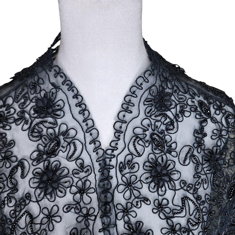 May include: Black beaded lace fabric with a floral design. The lace is delicate and intricate, with small black beads sewn throughout.