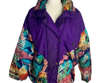 May include: A purple, multi-coloured, vintage ski jacket with a colourful abstract print on the sleeves and a solid purple body. The jacket has a zip closure and a snap button closure.