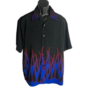 Puede incluir: Una camisa negra de manga corta con botones y un diseño de llamas azules y rojas en la parte inferior.