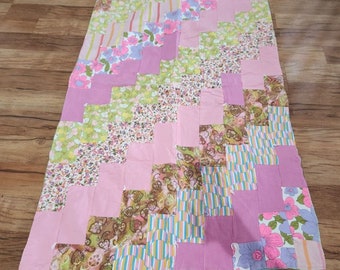 May include: A patchwork quilt with a pink, green, and brown color scheme. The quilt is made of various floral and geometric patterns.