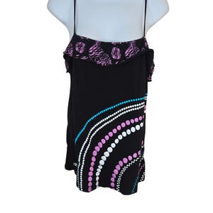 May include: Black tank top with spaghetti straps and a ruffled neckline. The top features a design of white, pink, and blue dots in an arc pattern. The neckline has a pink and black patterned design.