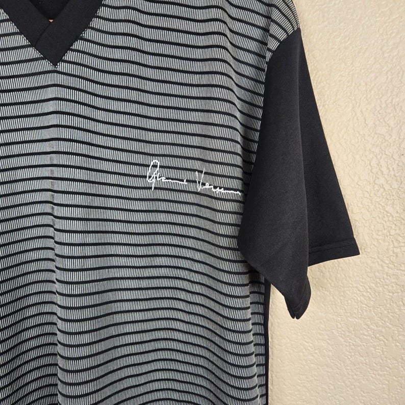 May include: A black and gray striped V-neck shirt with short sleeves. The shirt has a solid black sleeve and a white signature on the front. The shirt is made of a soft, comfortable material.