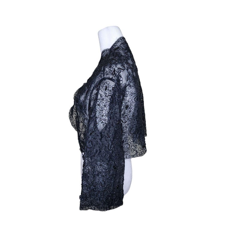 May include: A black lace shrug with a delicate floral pattern. The shrug has long sleeves and a cropped length.