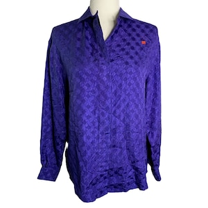 Puede incluir: Una blusa de manga larga de color morado con un patrón geométrico. La blusa tiene cuello y cierre de botones en la parte delantera.