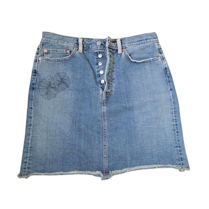 May include: Light blue denim skirt with a button-up front and a raw hem. The skirt features a floral embroidery design on the front. The skirt has five pockets and a classic denim look.