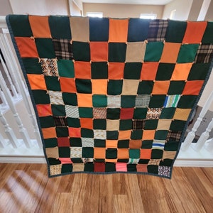 May include: A patchwork quilt with squares of orange, green, brown, and beige fabric. The quilt is made of different patterns and textures.