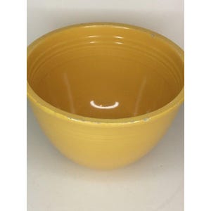 May include: A yellow ceramic bowl with a rounded shape. The bowl has a smooth, glossy finish and a slightly textured interior. The rim of the bowl shows some wear. The bowl is set against a white background.