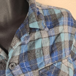 Puede incluir: Primer plano de una camisa a cuadros azul, gris y turquesa. La camisa tiene un bolsillo abotonado y un bot&oacute;n con el texto "PENDLETON SINCE 1863". La camisa est&aacute; hecha de una tela suave y tejida.