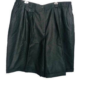 Op de afbeelding: Zwarte shorts met een geplooid voorpand, met knopen en zakken. De shorts hebben een hoge taille en een getailleerde pasvorm. De stof lijkt een donkere, effen kleur te hebben, mogelijk wol of een wolmix. De shorts hangen tegen een witte achtergrond.