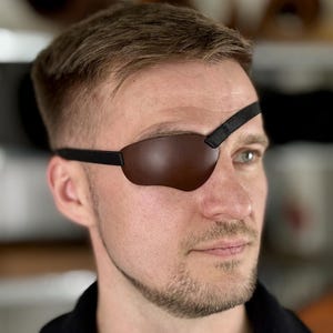 May include: A white ceramic mug with a black handle and the text "But First, Coffee" in a black, handwritten-style font. The mug is on a white surface.