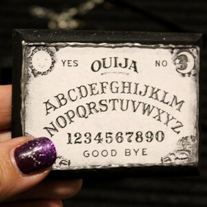 以下が含まれることがあります： 白地に黒枠のウィジャ盤。アルファベット、数字1から9と0、そして「YES」「NO」「GOOD BYE」の文字が書かれている。
