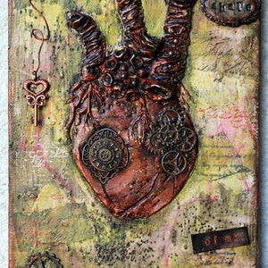 May include: A mixed media canvas featuring a textured, copper-coloured heart shape at the centre. The heart is decorated with gears, a keyhole, and the words "Shape of my". The background is a mottled yellow, green, and brown.
