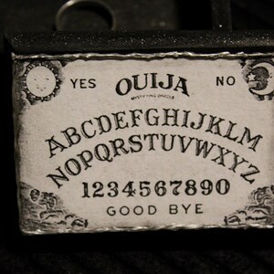 以下が含まれることがあります： 黒い枠と白い文字で書かれたヴィンテージスタイルのウィージャボード。ボードにはアルファベット、数字の1から9と0、