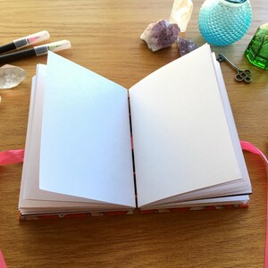 May include: An open blank journal with a pink ribbon bookmark. The journal has a colorful patterned cover.