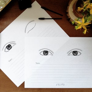 Puede incluir: Dos hojas blancas de papel con secciones rayadas para notas. Cada hoja tiene una ilustración en blanco y negro de un ojo con una ceja. La hoja superior tiene un solo ojo, mientras que la hoja inferior tiene dos ojos.