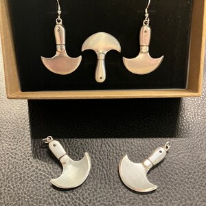 May include: A set of four silver earrings shaped like small knives. The earrings are displayed in a brown box with a black interior.