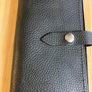 May include: Black leather wallet with a snap closure and a textured surface.