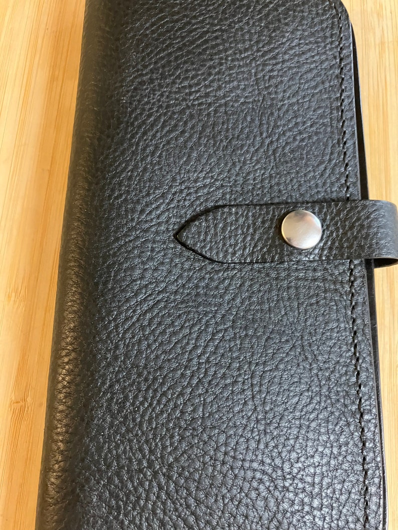 May include: Black leather wallet with a snap closure and a textured surface.