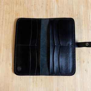 May include: Black leather wallet with multiple compartments and a snap closure. The wallet is open and the interior is visible.