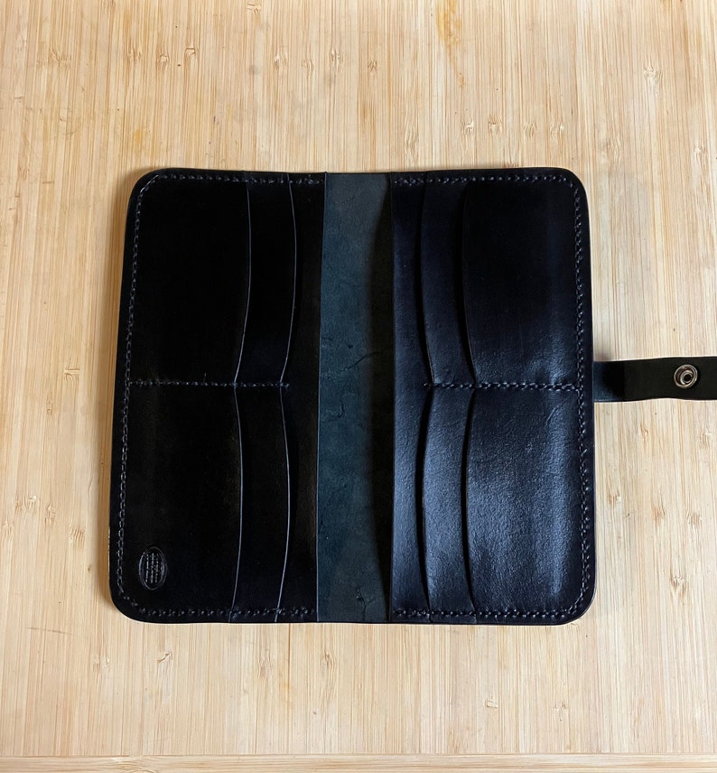 May include: Black leather wallet with multiple compartments and a snap closure. The wallet is open and the interior is visible.