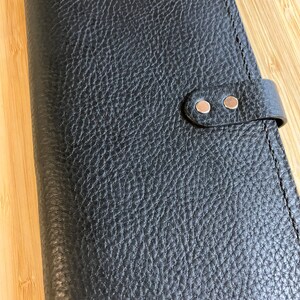 May include: Black leather wallet with a textured surface and two silver snaps on a strap.