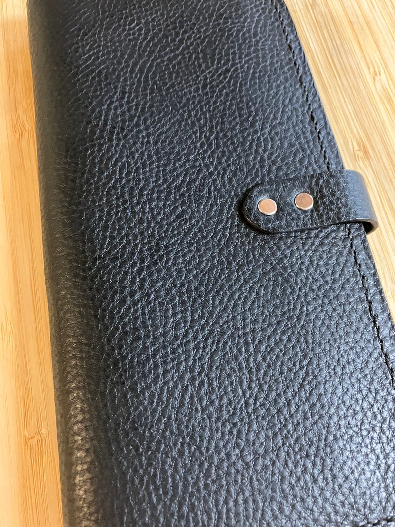 May include: Black leather wallet with a textured surface and two silver snaps on a strap.