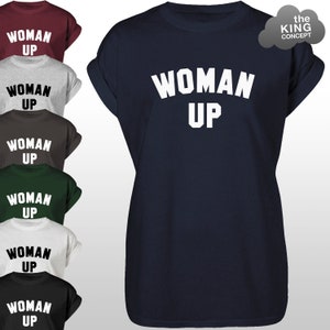 May include: A navy blue t-shirt with the text "WOMAN UP" in white letters. The shirt is shown in multiple colours, including maroon, grey, brown, green, white, and black.