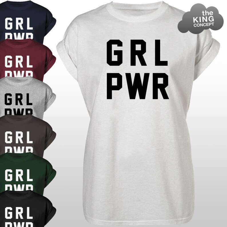 Pode incluir: Camiseta branca com a frase "GRL PWR" em letras pretas grandes. A imagem tamb&eacute;m mostra outras camisetas em azul marinho, bord&ocirc;, cinza, marrom, verde e preto, cada uma com a frase "GRL DWD". O logotipo The King Concept &eacute; vis&iacute;vel.