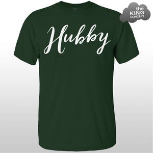 Może przedstawiać: Zielony T-shirt z napisem "Hubby" napisanym białym, ozdobnym pismem.