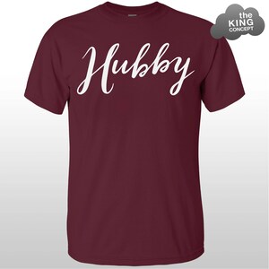 Może przedstawiać: Bordowy t-shirt z napisem "Hubby" napisanym białym, ozdobnym pismem.