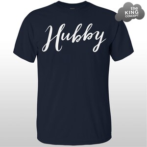 Może przedstawiać: Koszulka w kolorze granatowym z napisem "Hubby" napisanym białym, ozdobnym pismem.