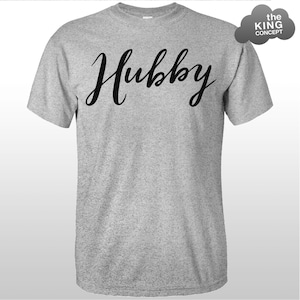 Może przedstawiać: Szary T-shirt z napisem "Hubby" napisanym czarnym, ozdobnym pismem.