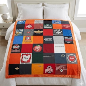 Puede incluir: Un edredón de retazos hecho con varias camisetas, con una mezcla de colores y logotipos. El edredón tiene un borde naranja y se muestra en una cama blanca. Los logotipos incluyen "Ohio State Buckeyes" y "Urban Farms".