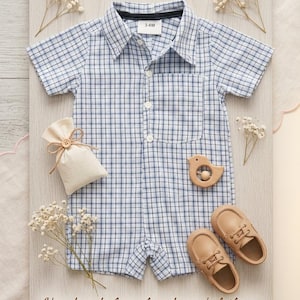 May include: A baby outfit set on a wooden board. The set includes a blue and white plaid romper, tan leather shoes, a wooden bird-shaped teether, and a small drawstring bag. The text "Handmade from loved ones' clothing" is visible.