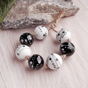 May include: A strand of black and white glass beads with a geometric pattern. The beads are strung on a natural twine cord.