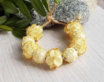 May include: A strand of yellow glass beads with a floral design. The beads are strung on a twine cord and are arranged in a circle.