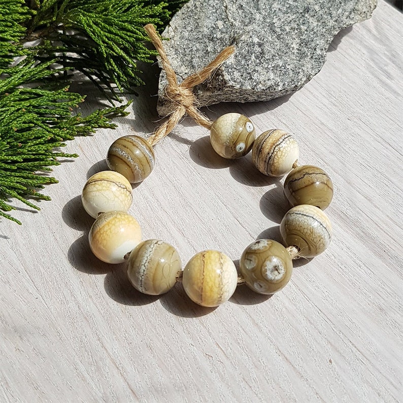 May include: A bracelet made of natural stone beads with brown and white stripes. The beads are strung on a natural twine cord.