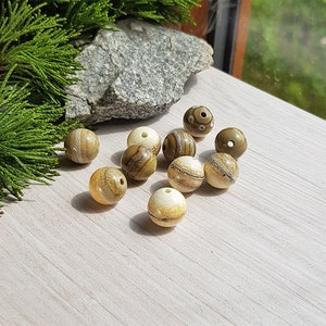 May include: A collection of round, brown and white striped beads with a natural, organic look. The beads are scattered on a light wood surface.