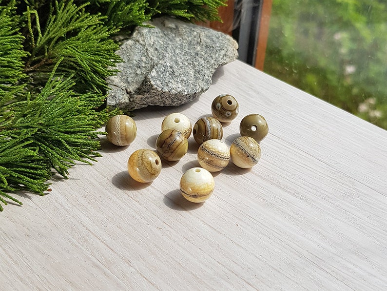 May include: A collection of round, brown and white striped beads with a natural, organic look. The beads are scattered on a light wood surface.