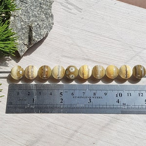 May include: A row of ten round, beige and brown agate beads with brown and white stripes, strung on a wire, measured on a ruler with inch markings.