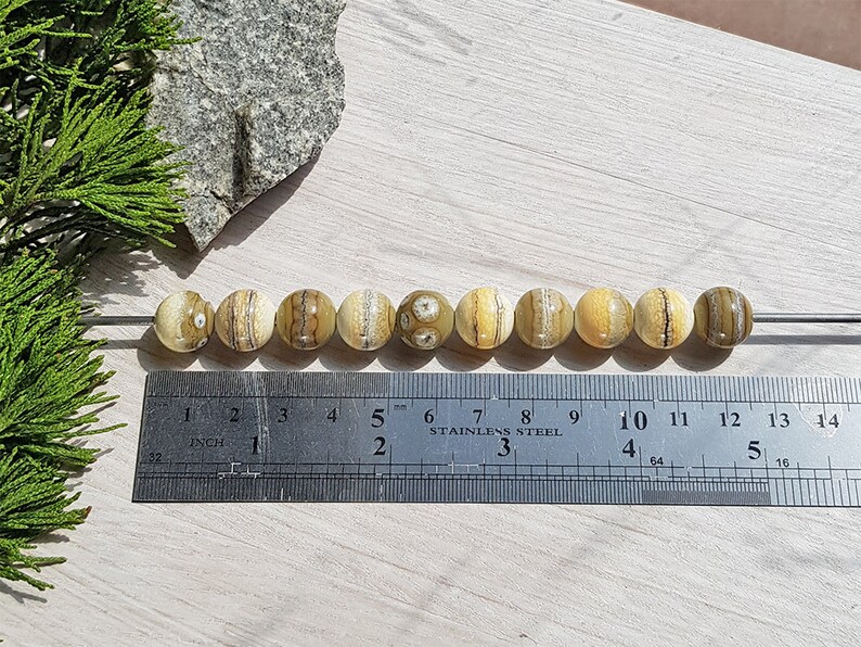May include: A row of ten round, beige and brown agate beads with brown and white stripes, strung on a wire, measured on a ruler with inch markings.