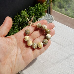 May include: A bracelet made of light brown and cream colored beads with a natural stone pattern. The beads are strung on a twine cord and tied together with a simple knot.